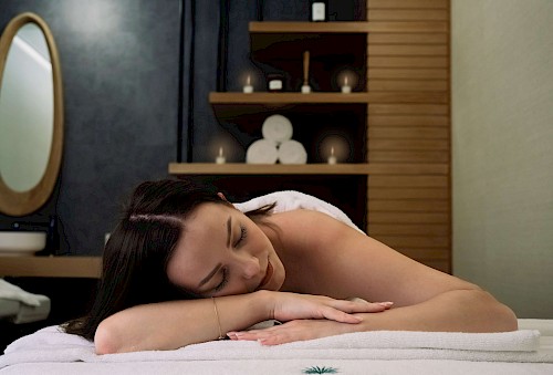 Junge Frau liegt entspannt auf einer Massageliege mit einem Handtuch auf dem Rücken